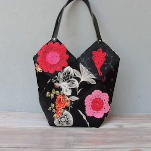 Puede incluir: Un bolso tote negro con un diseño floral y detalles de ganchillo. El bolso tiene un asa de cuero negro y está hecho de tela de patchwork.