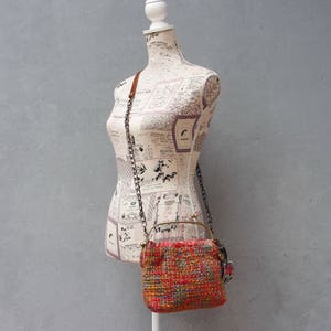 K&ouml;nnte beinhalten: Eine kleine, gewebte Handtasche mit einem rot-orange-blauen Muster. Die Tasche hat einen Messingrahmen und einen Kettenriemen.