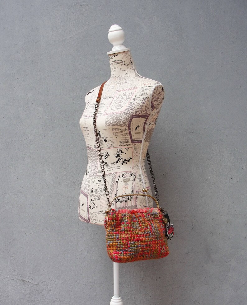 K&ouml;nnte beinhalten: Eine kleine, gewebte Handtasche mit einem rot-orange-blauen Muster. Die Tasche hat einen Messingrahmen und einen Kettenriemen.