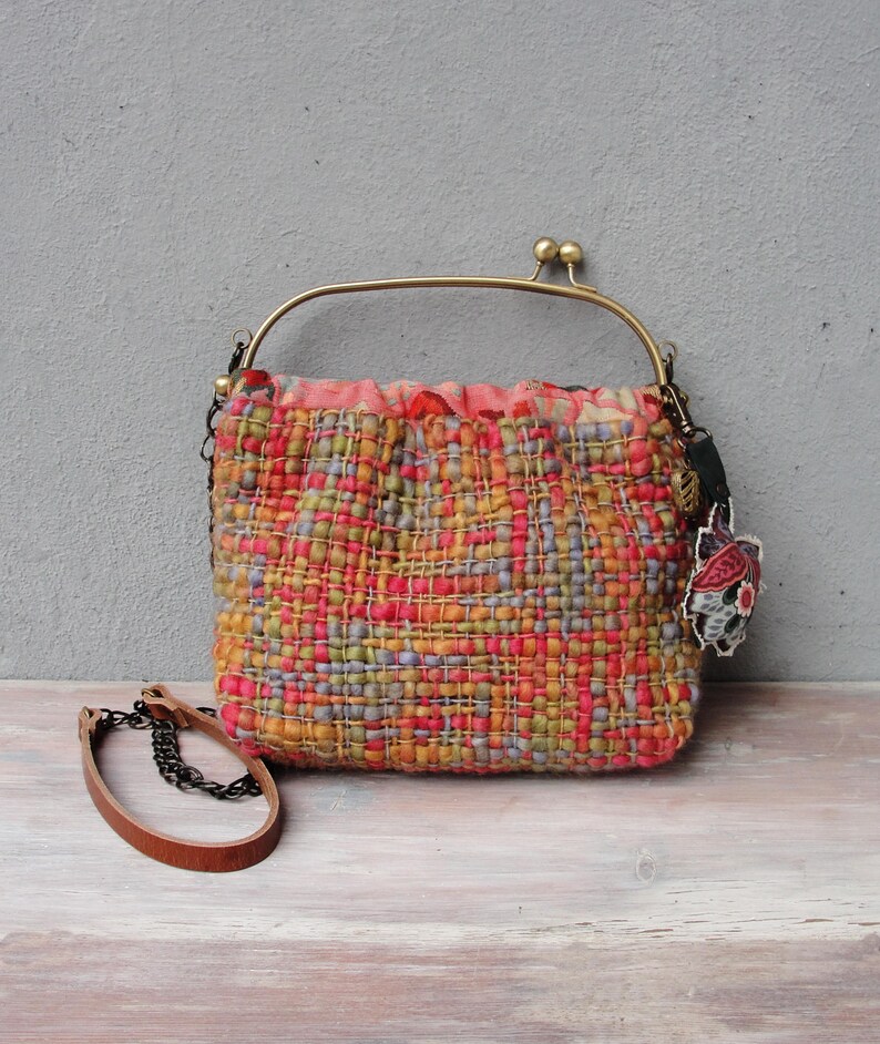 K&ouml;nnte beinhalten: Eine kleine gewebte Handtasche mit einem farbenfrohen geometrischen Muster in Orange-, Rosa-, Gr&uuml;n- und Blaut&ouml;nen. Die Tasche hat einen Messingrahmen und einen Kettenriemen.