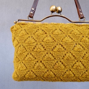 May include: Mustard yellow knitted handbag with a diamond pattern. The bag has a brass clasp and brown leather straps. The bag is approximately 10 inches wide and 7 inches tall.
