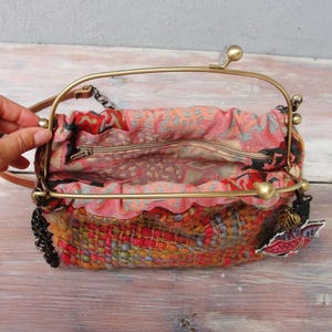 K&ouml;nnte beinhalten: Eine kleine, bunte gewebte Handtasche mit einem Messingrahmen und einem Kettenriemen. Die Tasche hat ein Blumenmuster und einen Rei&szlig;verschluss.