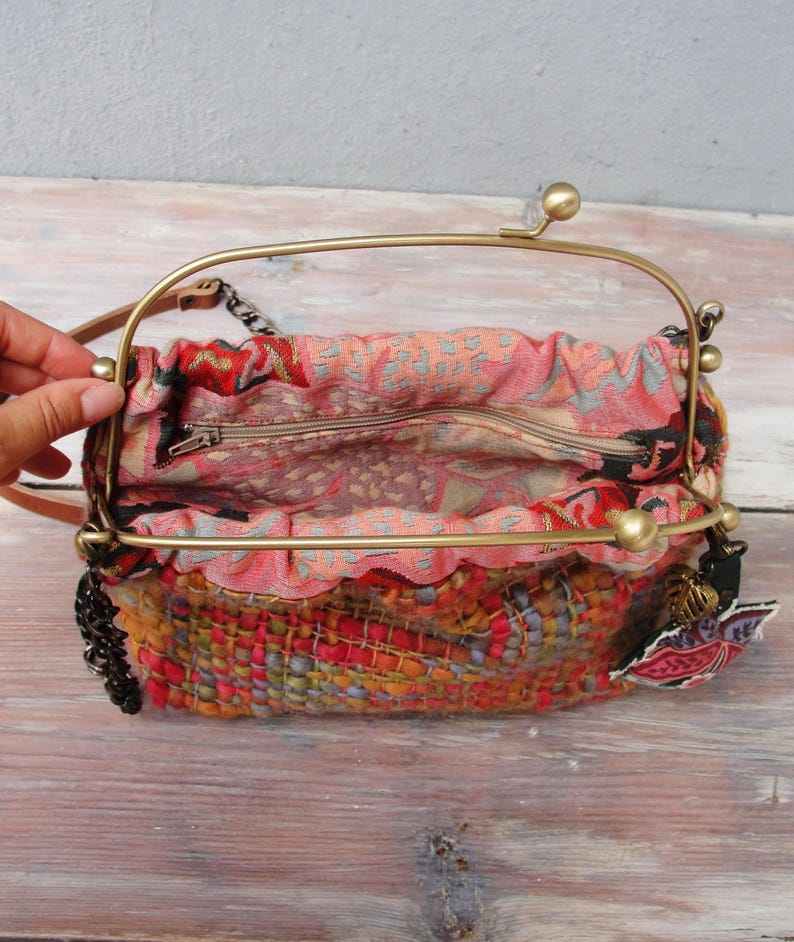 K&ouml;nnte beinhalten: Eine kleine, bunte gewebte Handtasche mit einem Messingrahmen und einem Kettenriemen. Die Tasche hat ein Blumenmuster und einen Rei&szlig;verschluss.