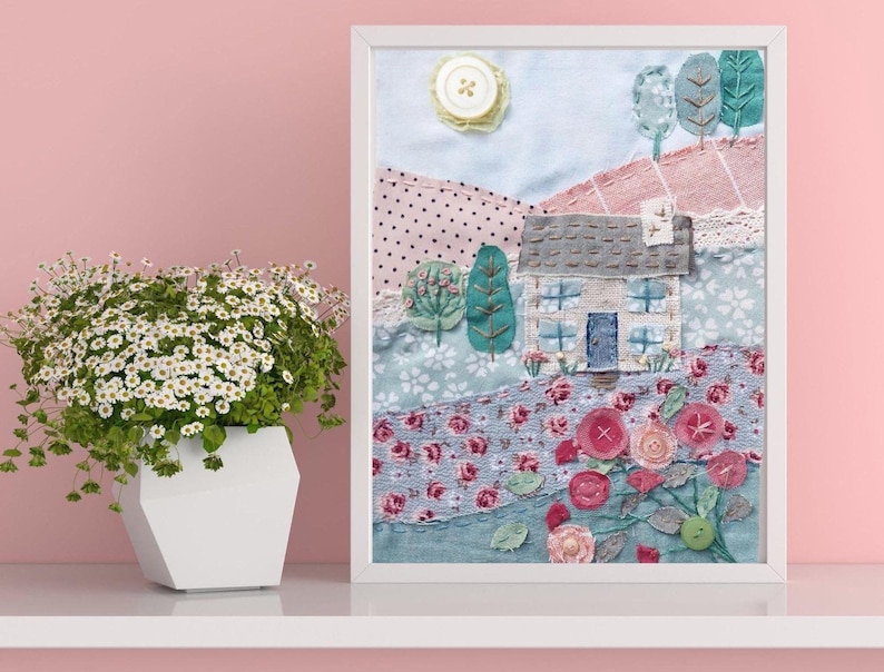 Image of Rose Cottage Slow  Stitch Kit completed in white frame. Natural fabric cottage with denim blue door pale blue windows and taupe roof. Set on fabric landscape of soft greens, floral prints, pink stripe and spot with stitched roses and trees.
