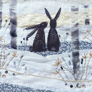 May include: Textile art piece featuring two dark gray rabbits in a winter scene. The artwork includes birch trees, embroidered details, and a snowy landscape with floral accents. The piece is predominantly white, gray, and beige.