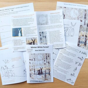 May include: A collection of printed instruction sheets for a "Winter White Forest" slow stitch kit. The sheets include patterns, stitch guides, and illustrations of rabbits and forest scenes. The color palette is primarily black, white, and gray.