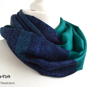 Könnte beinhalten: Ein türkisfarbener und marineblauer Seidenschal mit Paisley-Muster. Der Schal ist gefaltet und auf einer weißen Puppe ausgestellt.