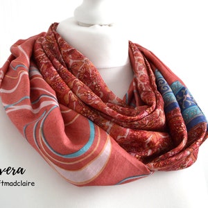Könnte beinhalten: Ein rot-blau-weiß gemusterter Schal mit Paisley-Muster. Der Schal ist zu einer Schleife gefaltet und wird auf einer weißen Puppe präsentiert. Der Text "Sixera by craftmadclaire" ist unter dem Schal gedruckt.