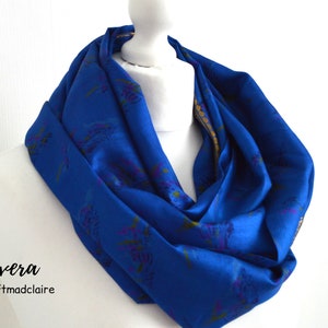 May include: A blue silk scarf with a floral pattern and gold trim. The scarf is folded and displayed on a white mannequin. The text "Sivera by craftmadclaire" is printed below the scarf.