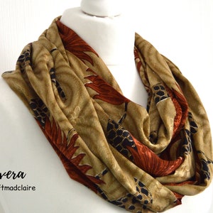 Könnte beinhalten: Ein brauner Infinity-Schal mit einem floralen Muster in Orange-, Schwarz- und Goldtönen. Der Schal ist aus einem weichen, komfortablen Stoff gefertigt und perfekt, um jedem Outfit einen Hauch von Stil zu verleihen.
