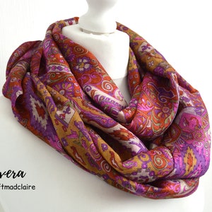 Könnte beinhalten: Ein farbenfroher Schal mit Paisley-Muster in den Farben Lila, Rosa, Orange und Braun. Der Schal ist gefaltet und um eine weiße Schaufensterpuppe gelegt.
