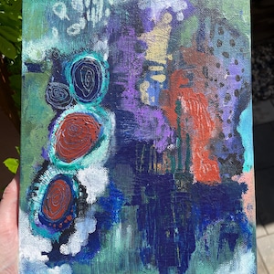 May include: Abstract painting on canvas with a mix of colors including teal, purple, red, and blue. The artwork features circular shapes with spiral details and textured brushstrokes, creating a dynamic and expressive composition.