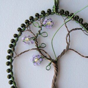 Close-up of a beaded frame, with a wire tree having green wire leaves and lilac beaded flowers applied