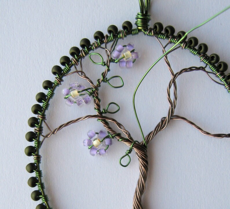 Close-up of a beaded frame, with a wire tree having green wire leaves and lilac beaded flowers applied