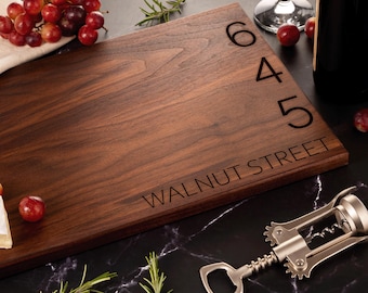 May include: A brown wooden cutting board with the address "645 Walnut Street" engraved on it. The board is surrounded by grapes, a corkscrew, and a bottle of wine.