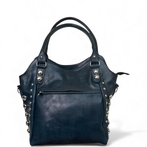 May include: A dark blue leather handbag with silver-colored stud accents. The bag has two top handles and a front zippered pocket. The bag is a tote style, with a structured shape and a slight curve at the top.