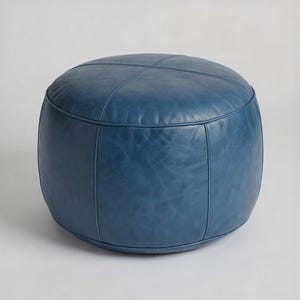 May include: A round, blue leather ottoman. The ottoman has a stitched cross pattern on top and vertical seams. The color is a deep, saturated blue with a slightly distressed appearance. The design is simple and modern.