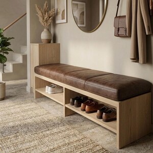 K&ouml;nnte beinhalten: Holz-Eingangsbank mit braunem Lederkissen und Schuhregalen. Die Bank ist aus hellem Holz gefertigt und hat mehrere Schuhpaare auf den Regalen. Eine Vase mit getrockneten Pflanzen steht auf einem passenden Holzschrank.