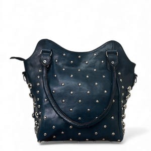 May include: A dark teal leather handbag with silver-colored studs. The bag has two handles and a curved top edge. The studs are evenly spaced across the surface of the bag.