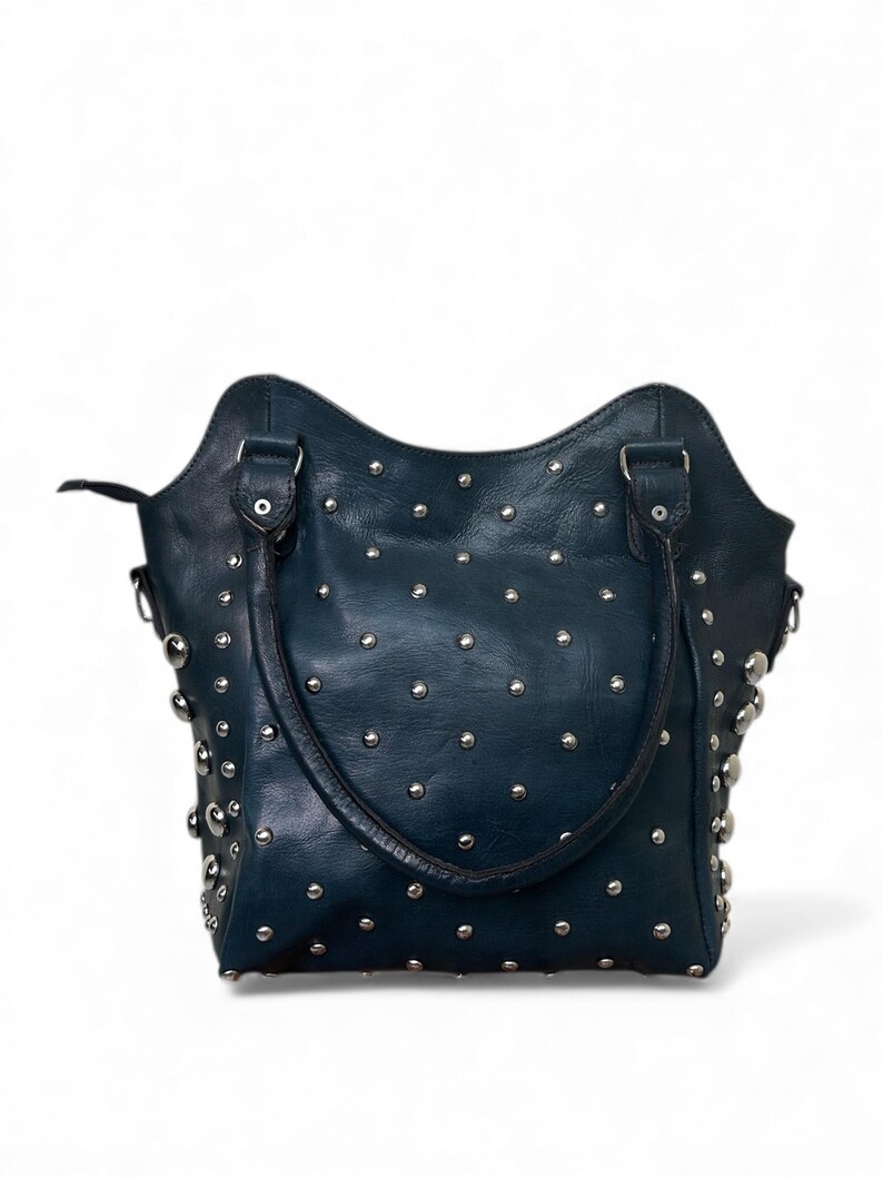 May include: A dark teal leather handbag with silver-colored studs. The bag has two handles and a curved top edge. The studs are evenly spaced across the surface of the bag.