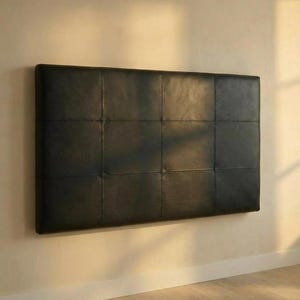 May include: A rectangular, black leather headboard with a grid pattern of stitched squares. The headboard is mounted on a light-colored wall, creating a minimalist aesthetic. The headboard is a piece of bedroom furniture.