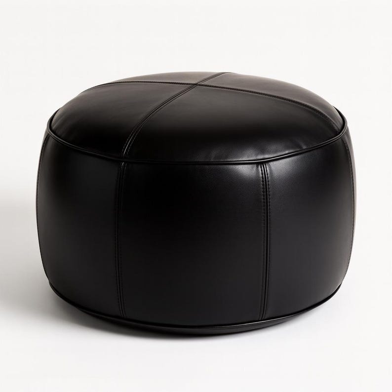 May include: A round, black ottoman with a stitched, cross-patterned top. The ottoman is made of a smooth, leather-like material and has a low profile. The sides are curved, and the base is a solid black.