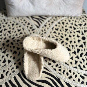 May include: A pair of white fluffy slippers with a soft, fuzzy texture. The slippers are on a black and white patterned surface.