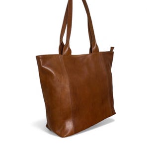 May include: A brown leather tote bag with two handles. The bag is rectangular with a zipper closure and a simple, classic design. The leather has a smooth texture and a warm, natural color.