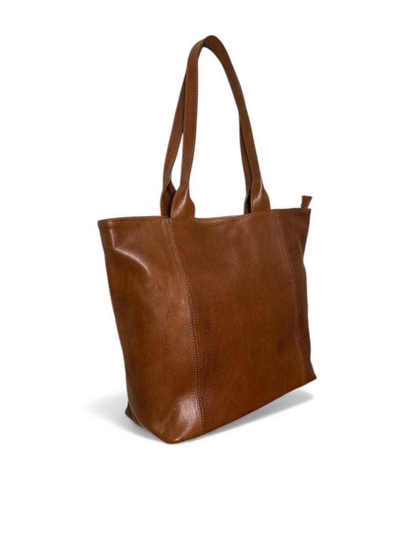 May include: A brown leather tote bag with two handles. The bag is rectangular with a zipper closure and a simple, classic design. The leather has a smooth texture and a warm, natural color.