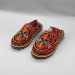 Puede incluir: Un par de zapatos de cuero rojo con coloridos patrones geométricos bordados. Los zapatos tienen una suela blanca y un detalle de costura blanca alrededor del borde.