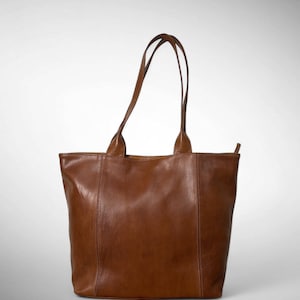 May include: A brown leather tote bag with two handles. The bag has a rectangular shape with a vertical seam down the front and back. The handles are attached to the top of the bag and are made of the same brown leather.