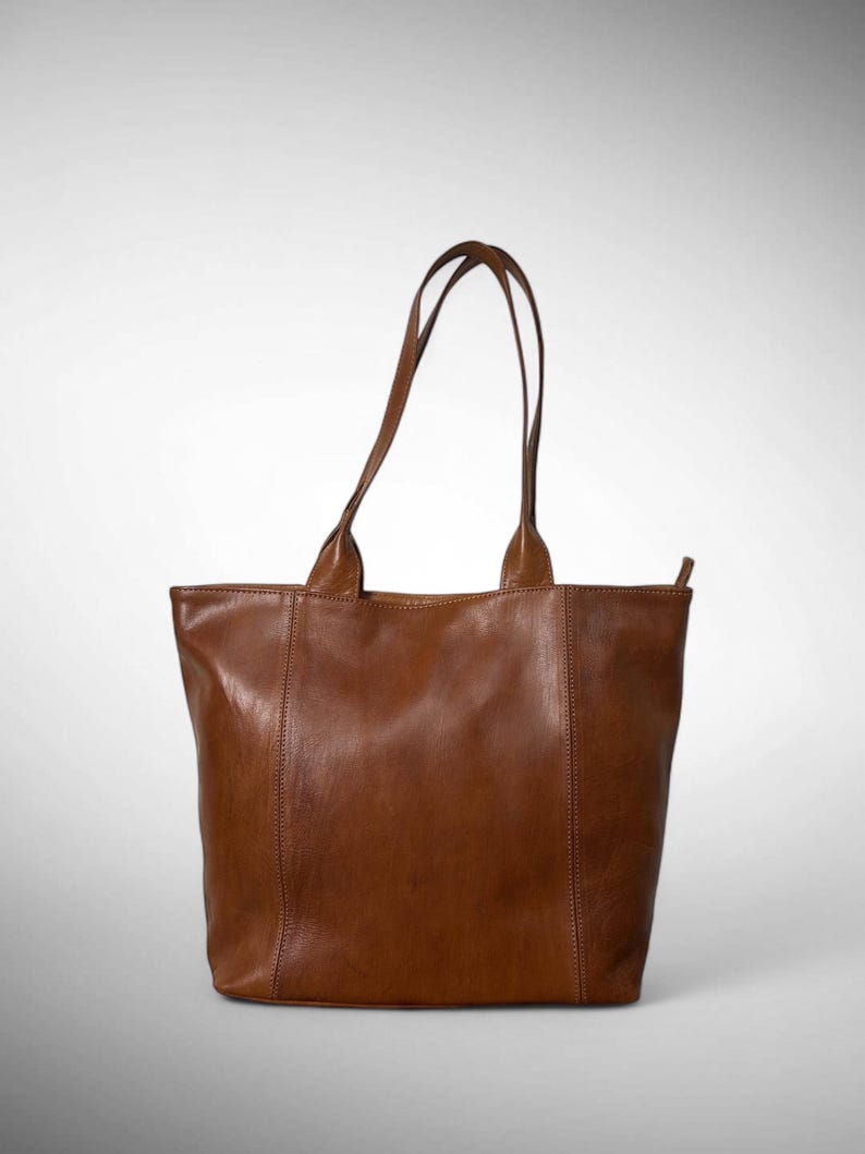 May include: A brown leather tote bag with two handles. The bag has a rectangular shape with a vertical seam down the front and back. The handles are attached to the top of the bag and are made of the same brown leather.