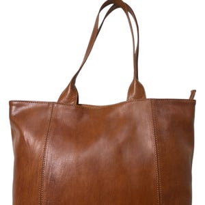 May include: A brown leather tote bag with two long handles. The bag has a rectangular shape with vertical seams on the front and back. The leather has a smooth texture and a warm, natural color.
