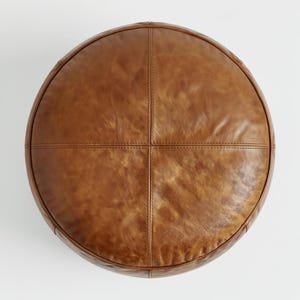 Peut inclure: Un pouf rond en cuir marron avec un design cousu. Le pouf est divis&eacute; en quatre sections par des coutures. Le cuir a un aspect l&eacute;g&egrave;rement vieilli, avec des variations de couleur et de texture.