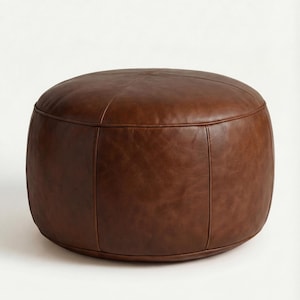 May include: A brown leather ottoman with a rounded, cylindrical shape. The ottoman has a stitched seam detail and is made of a smooth, dark brown leather. It is a comfortable and stylish piece of furniture.