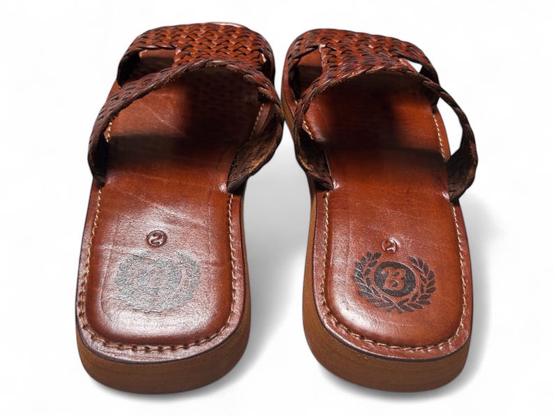 May include: Pair of brown leather sandals with woven straps. The sandals have a rounded toe and a thick sole. The footbed is stamped with a number and a logo. The sandals are a size 9.