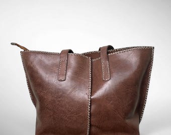May include: A brown leather tote bag with two handles and a stitched design. The bag has a rectangular shape and a spacious interior. The stitching is white, and the bag is made of a durable material.