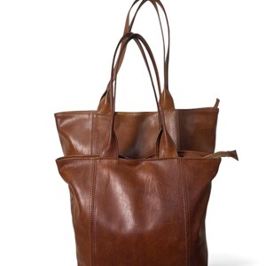 May include: Two brown leather tote bags with long handles. The bags are a medium brown color and appear to be made of a soft, supple leather. The bags have a simple, classic design, with a rectangular shape and a zipper closure.