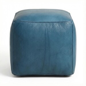 May include: A square, teal-colored ottoman with a leather-like texture. The ottoman has a simple, modern design and is suitable for use as a footrest or extra seating. The color is a deep, muted teal.
