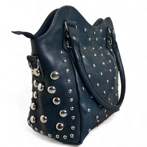 May include: A teal handbag with silver-colored studs. The bag has a structured shape with a top handle and a shoulder strap. The studs are evenly spaced across the front, sides, and back of the bag, adding a decorative element to the design.