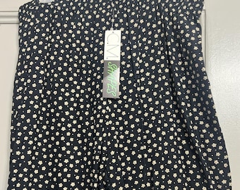 Puede incluir: Pantalones negros con estampado floral blanco. Los pantalones están colgados de una percha. Una etiqueta que dice "CM Shapes" está adjunta a los pantalones.