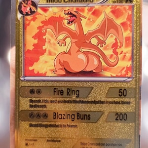 May include: A gold-colored trading card featuring a cartoon Charizard with the text "Thicc Charizard". The card has "Fire Ring" and "Blazing Buns" attack descriptions, with a HP of 120.