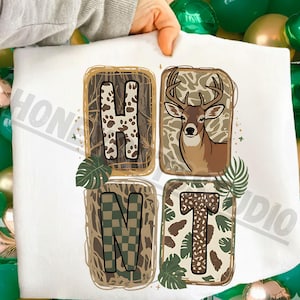 Puede incluir: Tela blanca con la palabra "HUNT" en un diseño cuadrado. Las letras están rellenas de patrones de camuflaje y una ilustración de ciervo. Hojas verdes se colocan alrededor de las letras. La palabra "HONEY STUDIO" está impresa en la tela.
