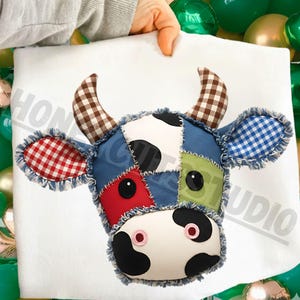May include: A patchwork cow head with a white face, black spots, and a red button nose. The ears are red and blue gingham, and the horns are brown and white checkered. The cow head is held up by a person.