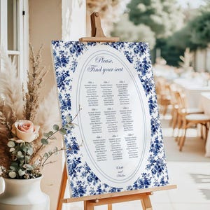 Peut inclure: Un plan de table de mariage floral bleu et blanc avec le texte "Please. Find your seat." dans un ovale blanc. Le tableau est sur un chevalet.