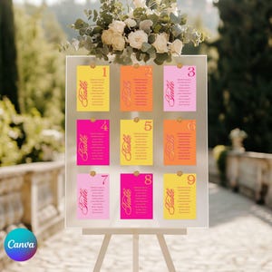 May include: A clear acrylic seating plan with nine colourful cards, each numbered and listing names. The cards are in shades of yellow, orange, and pink, with gold text and attached with gold pins. A floral arrangement sits above the chart.