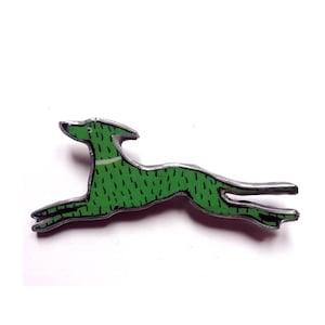 Op de afbeelding: Een groene emaille pin van een gestileerde rennende hond. De hond is zilverkleurig omrand en heeft een witte streep om zijn nek.