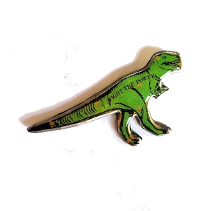 Può includere: Un apribottiglie a forma di dinosauro verde con le parole "Fight the Power" stampate sul lato. Il dinosauro è in metallo e ha una finitura lucida.