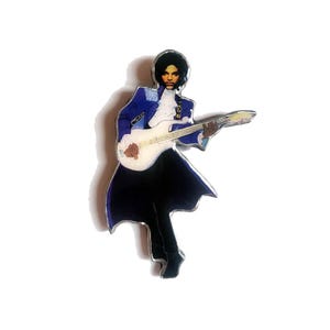 May include: A pin depicting a musician playing a white guitar. The musician is dressed in a blue jacket with white details, a white ruffled shirt, and black trousers. The pin has a silver edge.