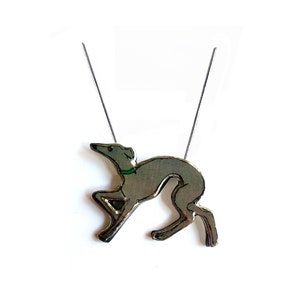 May include: A silver necklace with a grey and white dog pendant. The dog is wearing a green collar.